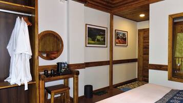 Habitación de hotel con cama, escritorio de madera con cafetera, espejo y perchero.