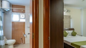 Ein Hotelzimmer mit Holztür, einem Bett mit grünen Kissen, einer weißen Toilette, einer Duschkabine und einem Fenster.