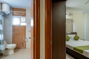 Ett hotellrum med en trädörr, en säng med gröna kuddar, en vit toalett, en dusch och ett fönster.