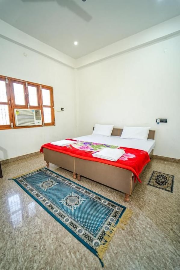 A bedroom with a bed, a window, a wall-mounted air conditioner, and a patterned rug.