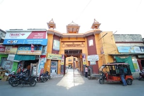 A street view with a yellow building featuring multiple auto trader signs, a motorcycle parked in front, and a rickshaw on the right.