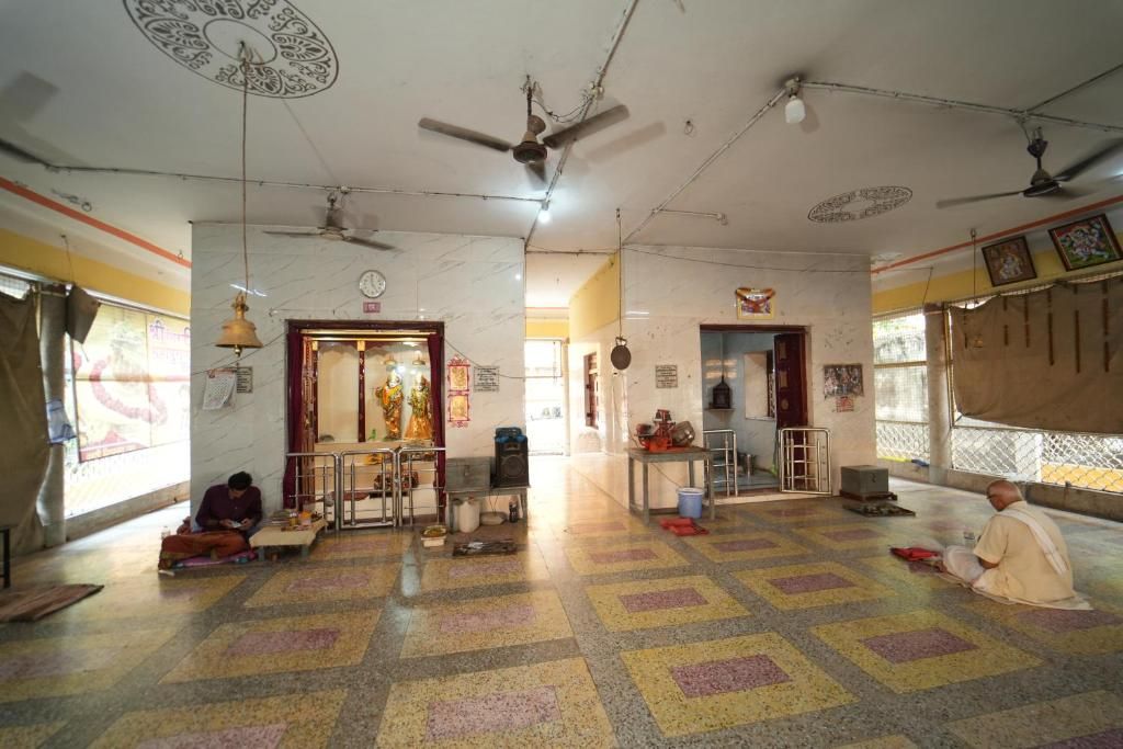 A room with a patterned floor, ceiling fans, a clock, and a person sitting on the floor.