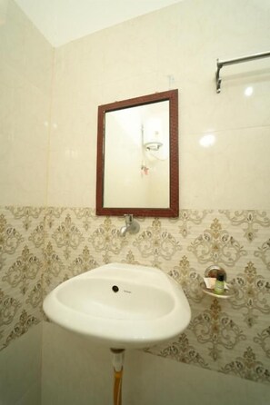 A bathroom with a pedestal sink, a mirror with a wooden frame, and patterned wall tiles.