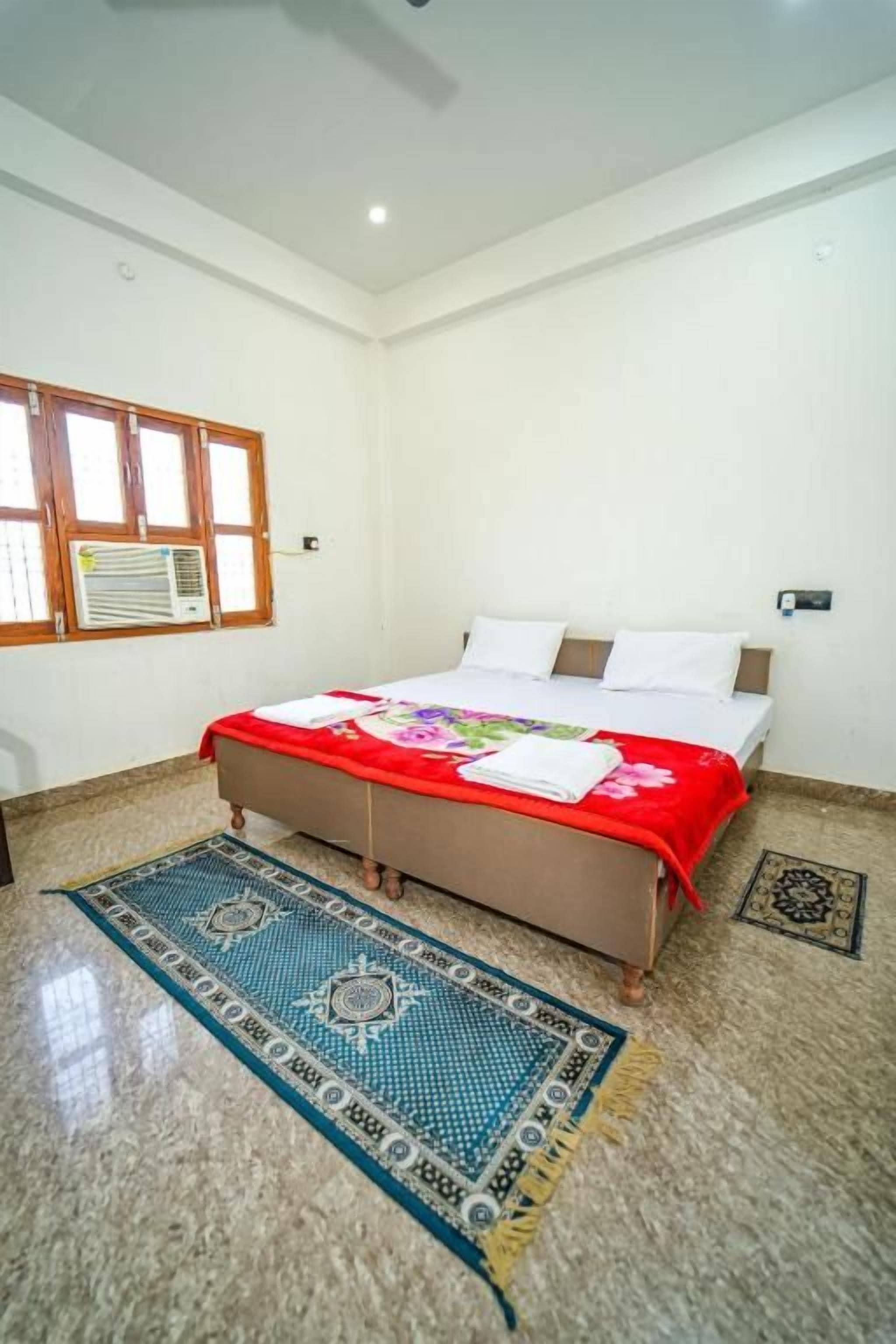 A bedroom with a bed, a window, a wall-mounted air conditioner, and a patterned rug.