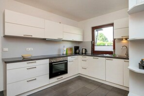 A modern kitchen with white cabinets, a black oven, and a window providing natural light. - Holiday home with 1 bedroom (Zingst (Ostseeheilbad))