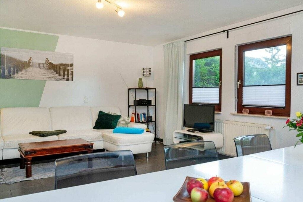 A modern living room with a white sofa, a glass coffee table, a television, and a dining area with a table and chairs.