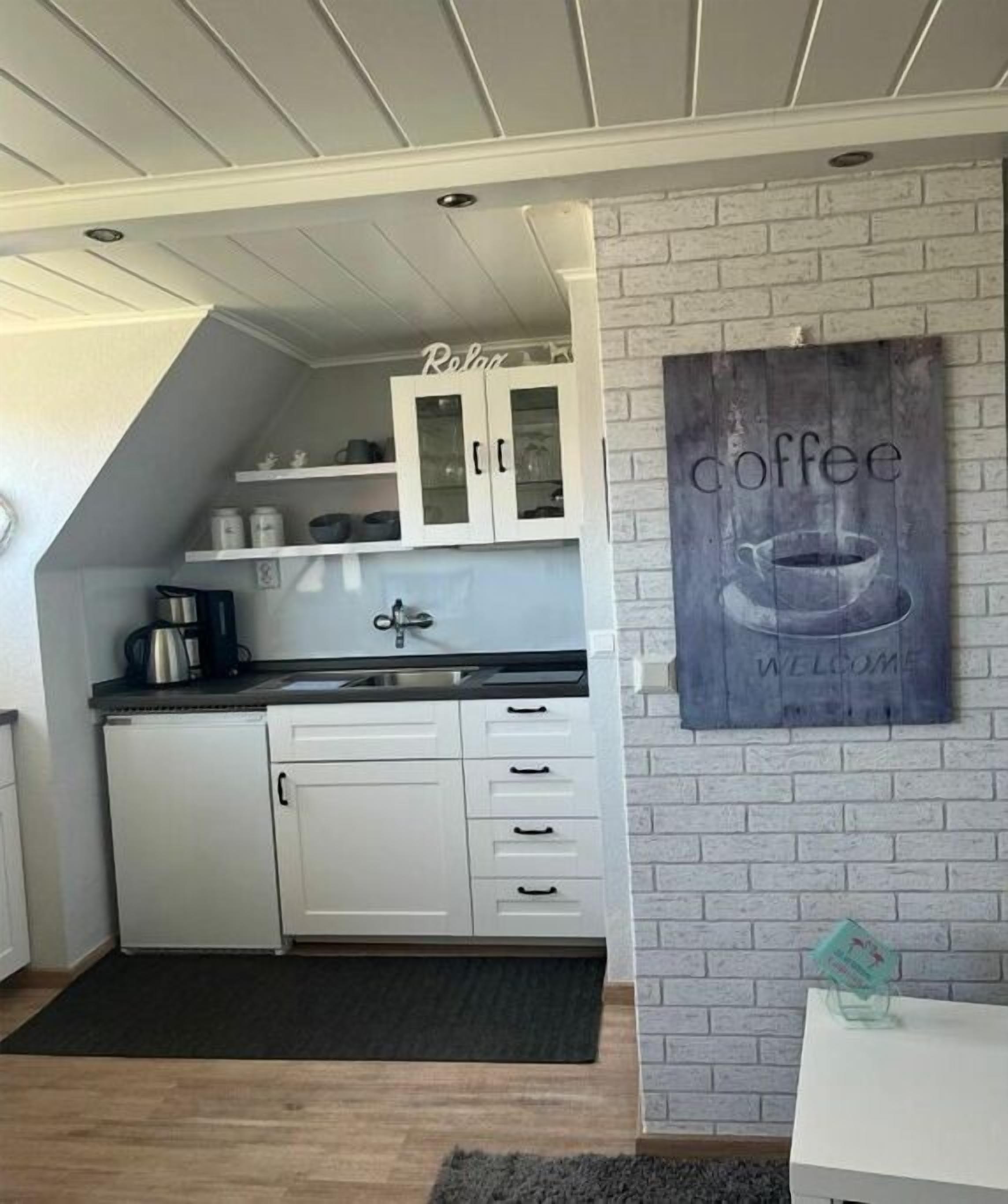 A kitchen with white cabinets, a black countertop, and a coffee-themed welcome sign.