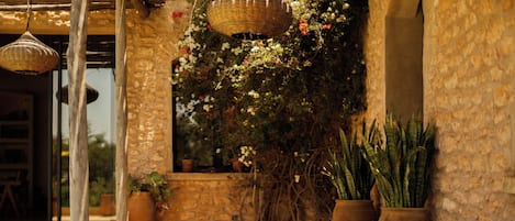 An outdoor seating area with a stone wall, a woven ceiling light, and potted plants.