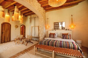 Quarto rústico com parede de pedra, móveis de madeira, cama com roupa de cama listrada e luminárias pendentes.