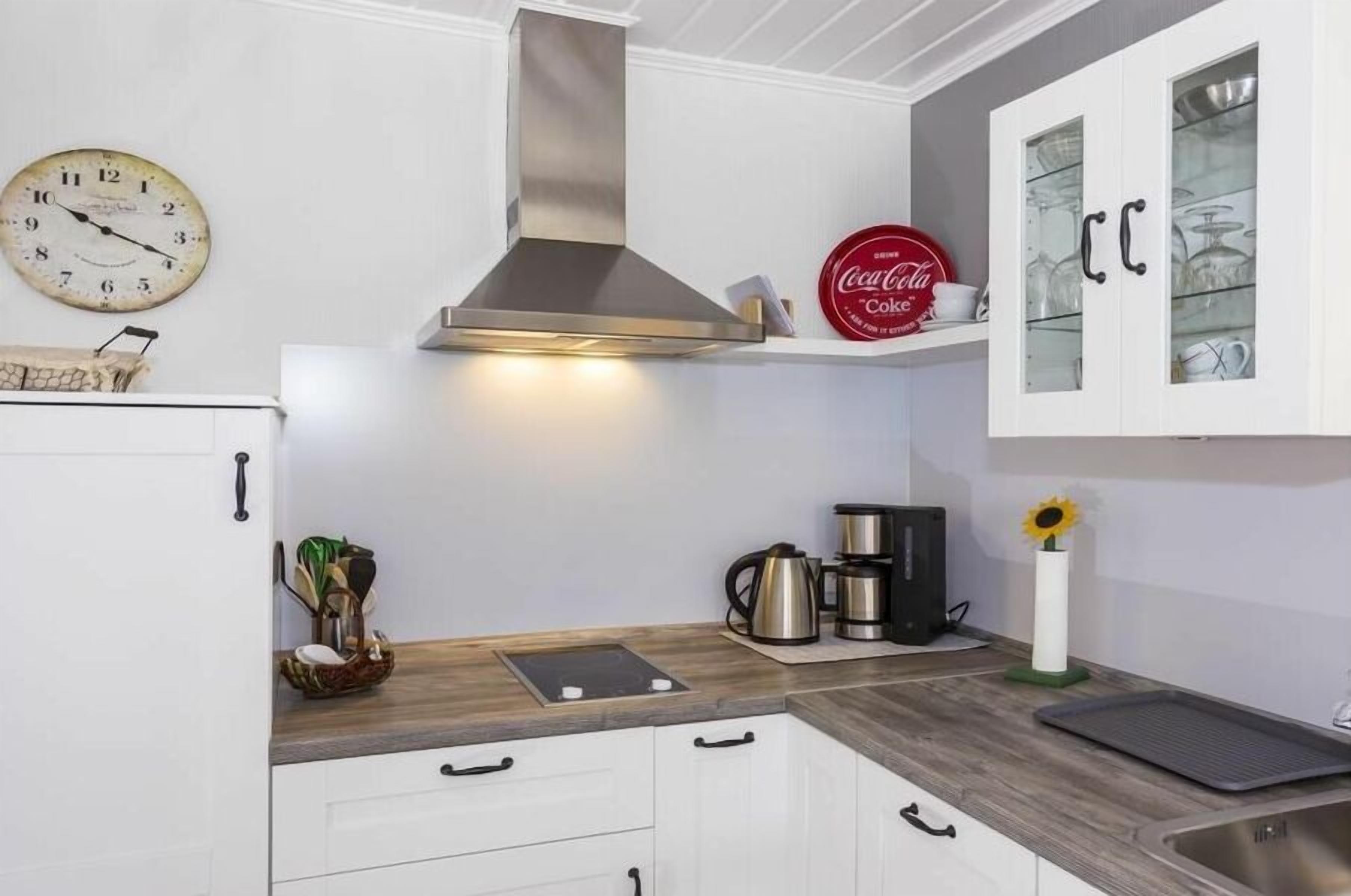 A kitchen with white cabinets, a stainless steel range hood, a clock, a Coca-Cola sign, and a coffee maker.