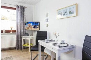 A room with a television, a dining table set for two, a chair, and a radiator. - Holiday apartment with 1 bedroom (Zingst)