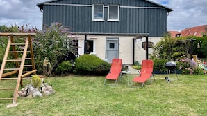 A two-story house with a dark exterior, a front door, and a small porch area with two red chairs and a table. - Vrbo Property (Velgast)