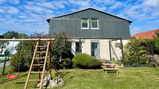 A house with a dark roof and white walls, a small garden with a bench, and a swing set. - Vrbo Property (Velgast)