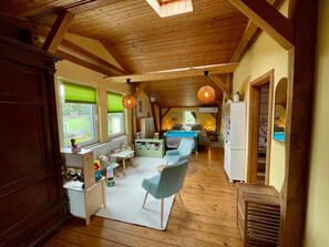Un intérieur chaleureux avec un plafond en bois, un coin repas comprenant une table et des chaises, et une vue sur l’extérieur grâce à de grandes fenêtres.