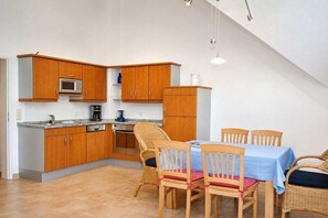 Eine kleine Küche mit Holzausstattung, einer Mikrowelle und einem Essbereich mit Korbstühlen und einer blauen Tischdecke.