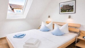 A bedroom with a bed, pillows, a bedside table, a nightstand, a window, and a picture on the wall. - Residence Am Strand 1-16 (Seeheilbad Zingst)