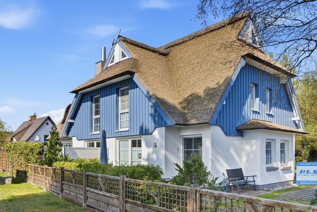 Une maison traditionnelle avec un toit à forte pente, un toit de chaume et une clôture en bois à l’avant.