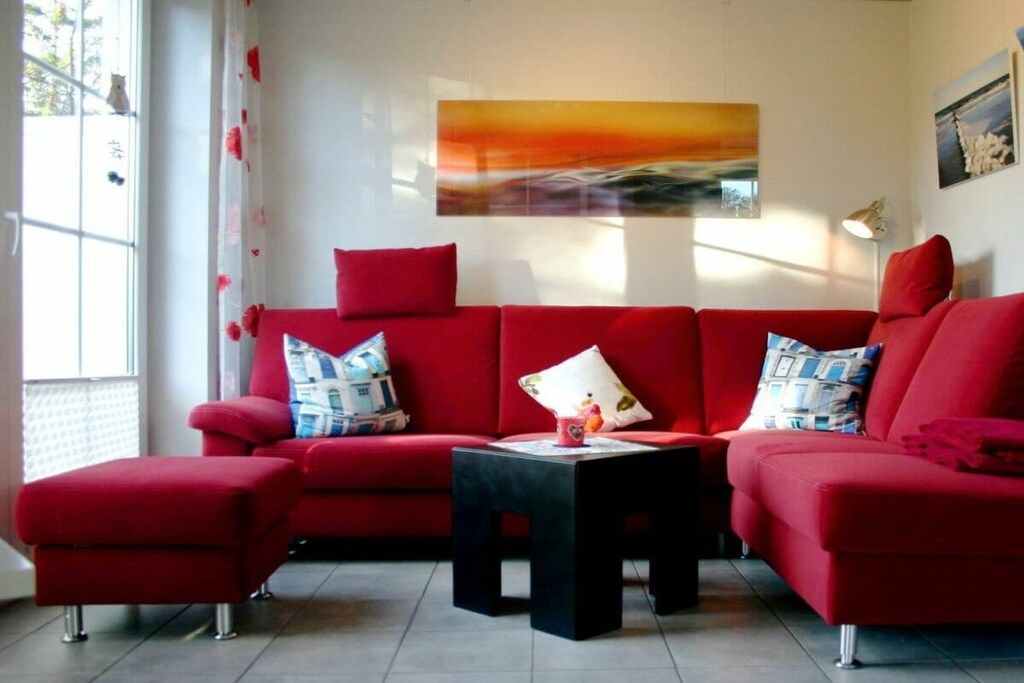 Eine rote Sofagarnitur mit einem schwarzen Couchtisch in einem Zimmer, das ein großes Fenster, ein Wandbild und eine Lampe beinhaltet.