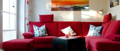 A red sofa set with a black coffee table in a room with a large window, a painting on the wall, and a lamp.