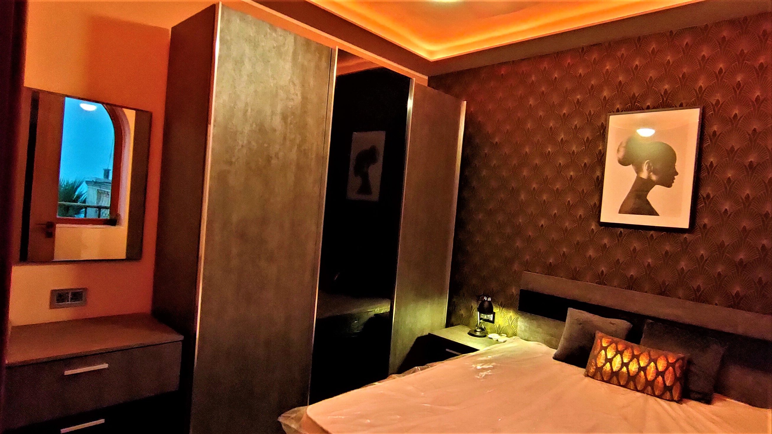 Quarto de hotel com cama, mesa de cabeceira, espelho e um quadro na parede.