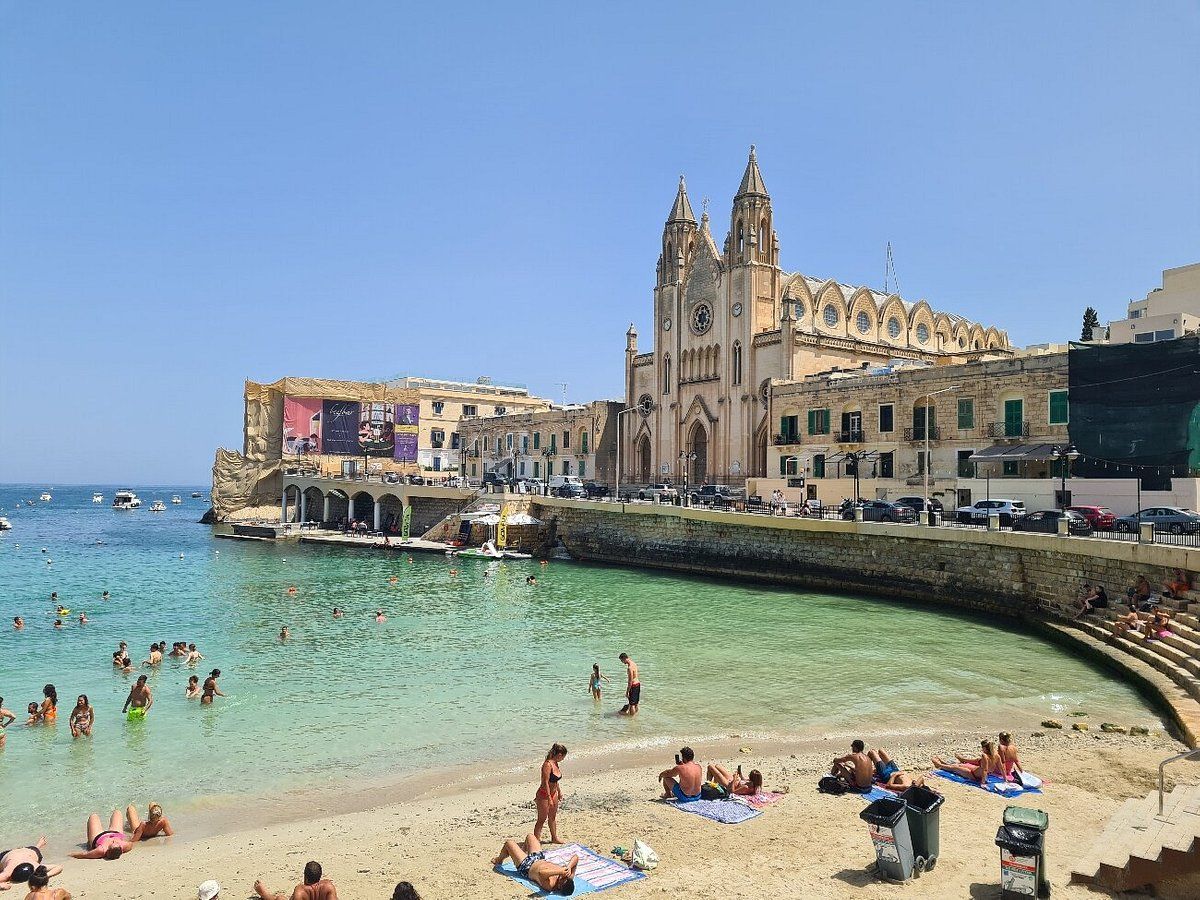 A coastal town with a prominent church, clear waters, and a sandy beach.
