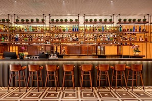 Zona de bar con estantes llenos de botellas de licores, taburetes y una barra con una computadora portátil.