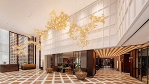 Een ruime lobby met een zwart-wit geruit vloerpatroon, grote ramen en decoratieve verlichtingsarmaturen.