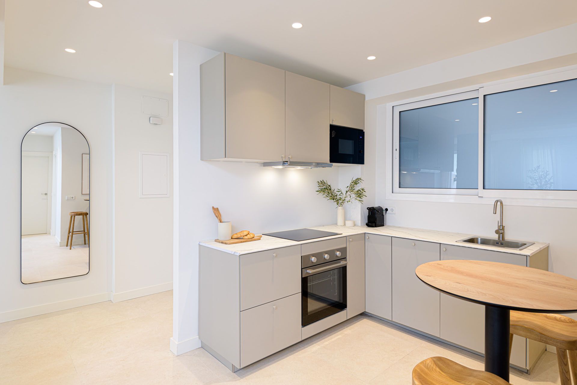 A modern kitchen with a built-in oven, a window, and a round table.