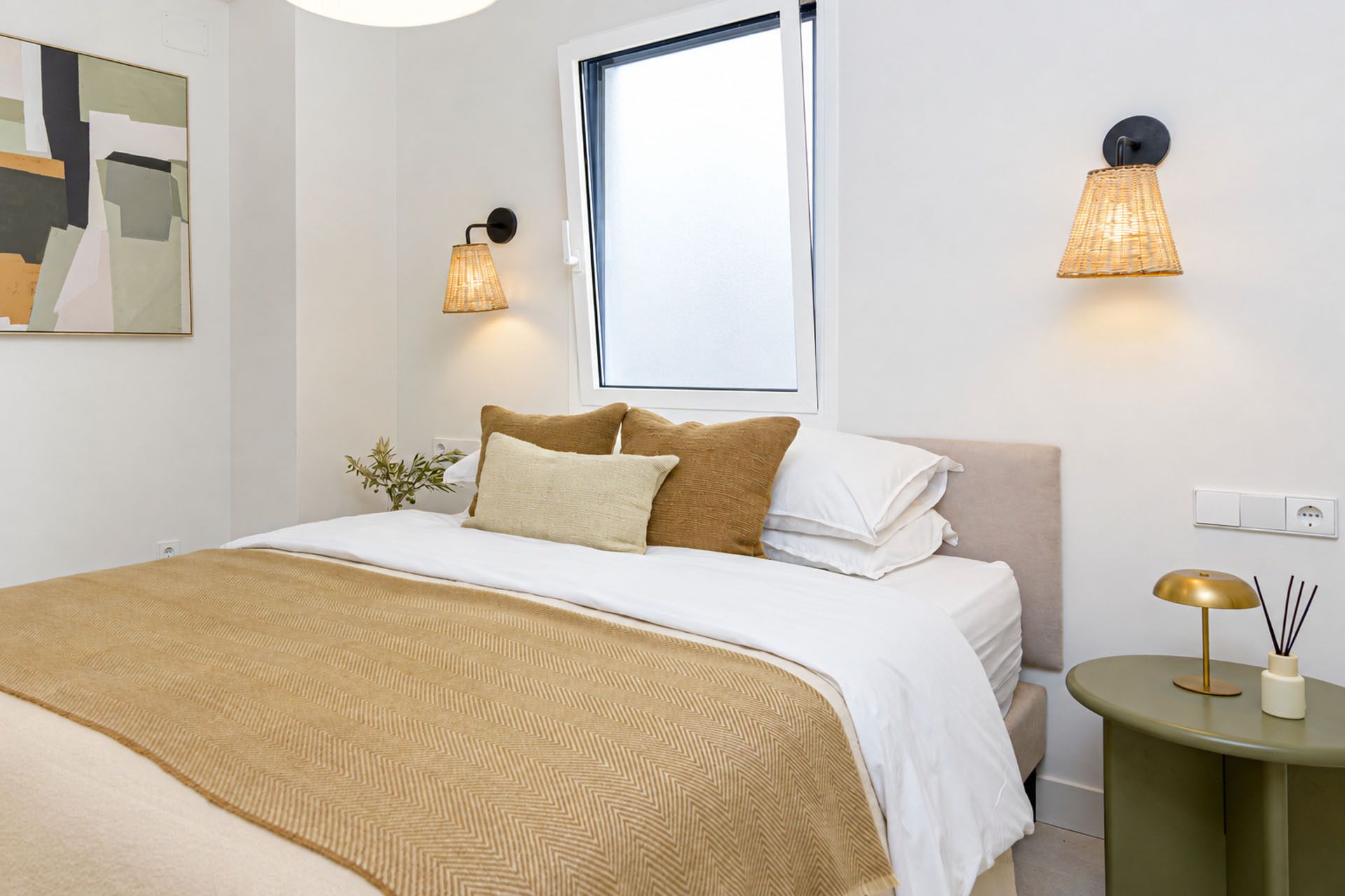 Una camera da letto ordinata con un letto, cuscini, un comodino e lampade a parete.