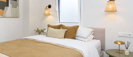 A neatly arranged bedroom with a bed, pillows, a bedside table, and wall-mounted lamps.