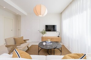 A modern living room with a sofa, a coffee table, a TV, and a large window with sheer curtains. - Victoria - Holiday Apartment in Malaga (Málaga)