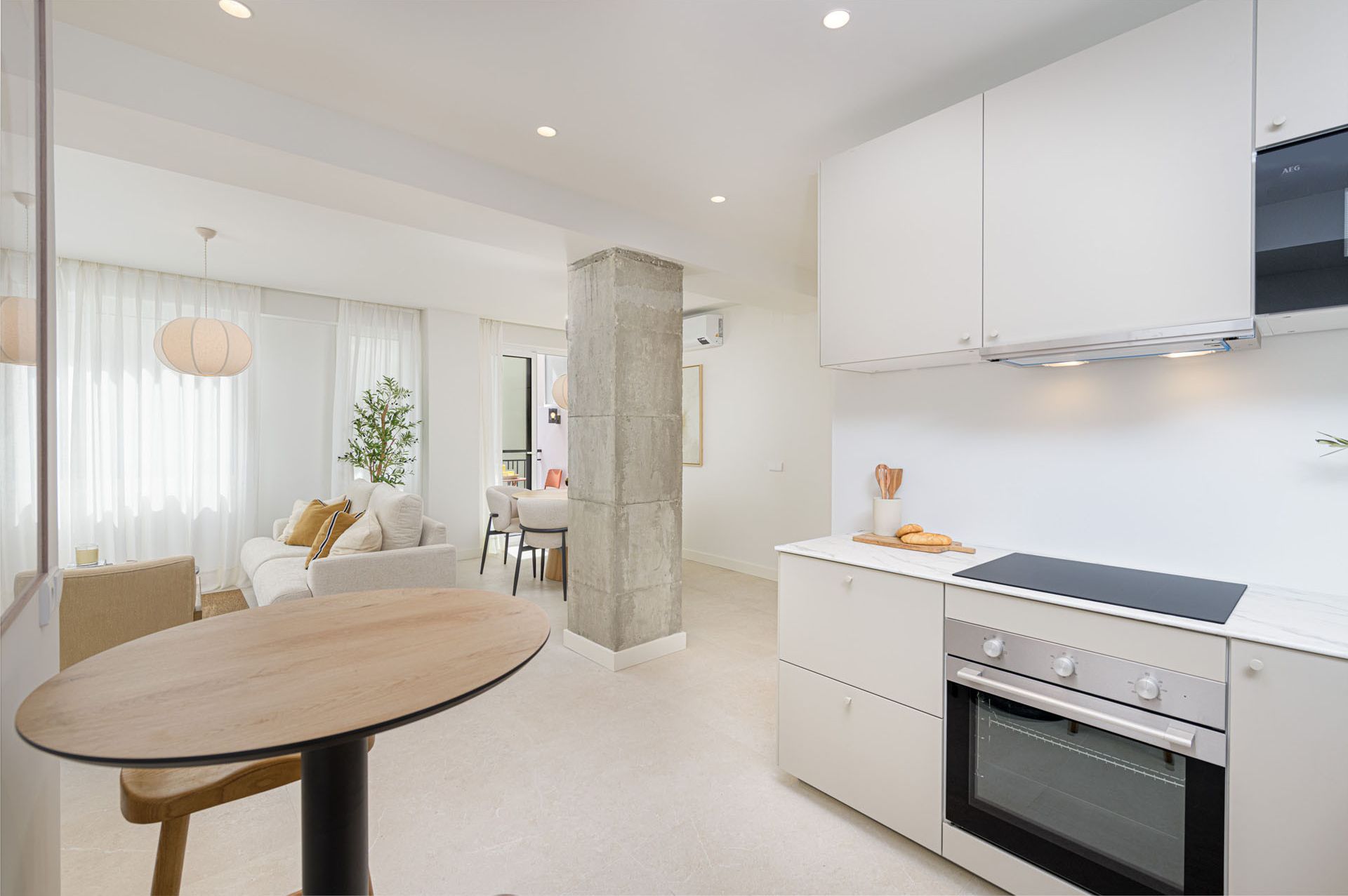 A modern kitchen with a built-in oven, a dining area with a round table, and a living space with a sofa and curtains.