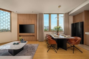 A modern living room with a flat-screen TV, a dining area with a marble table, and a large window offering a city view.