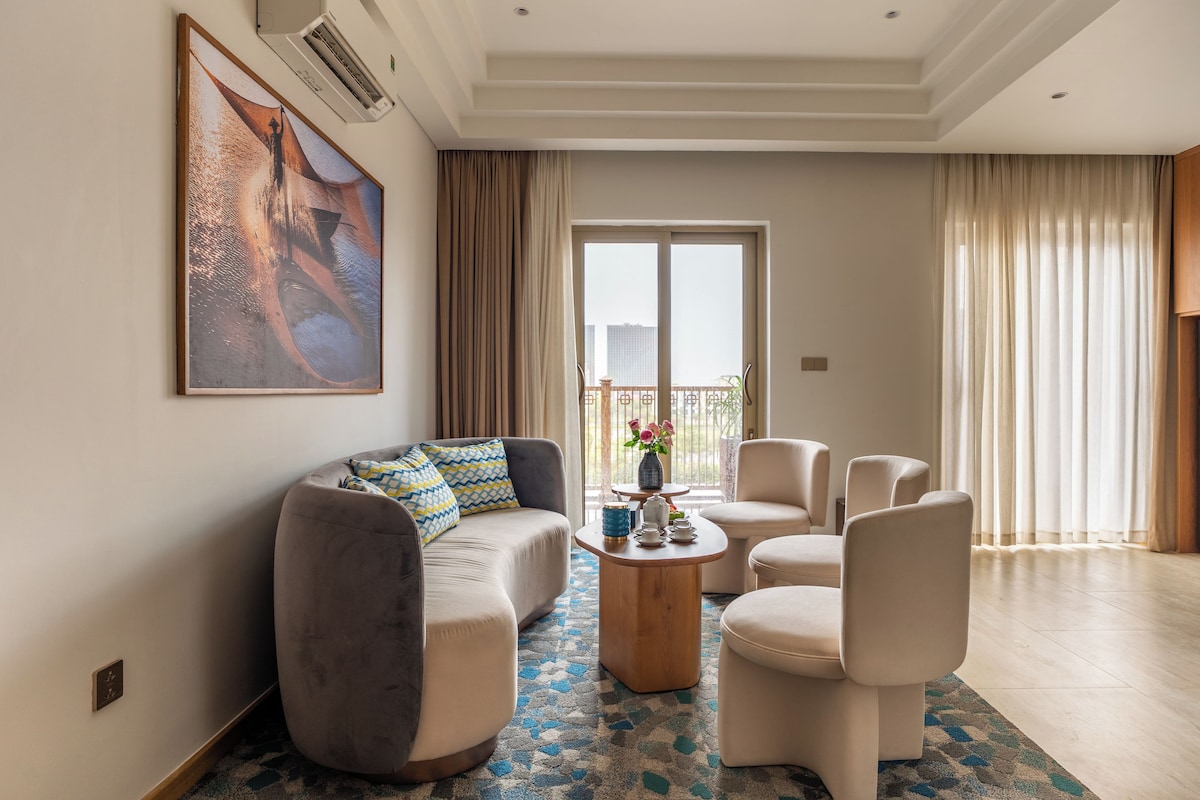A modern living room with a sofa, chairs, a coffee table, and a large painting on the wall.