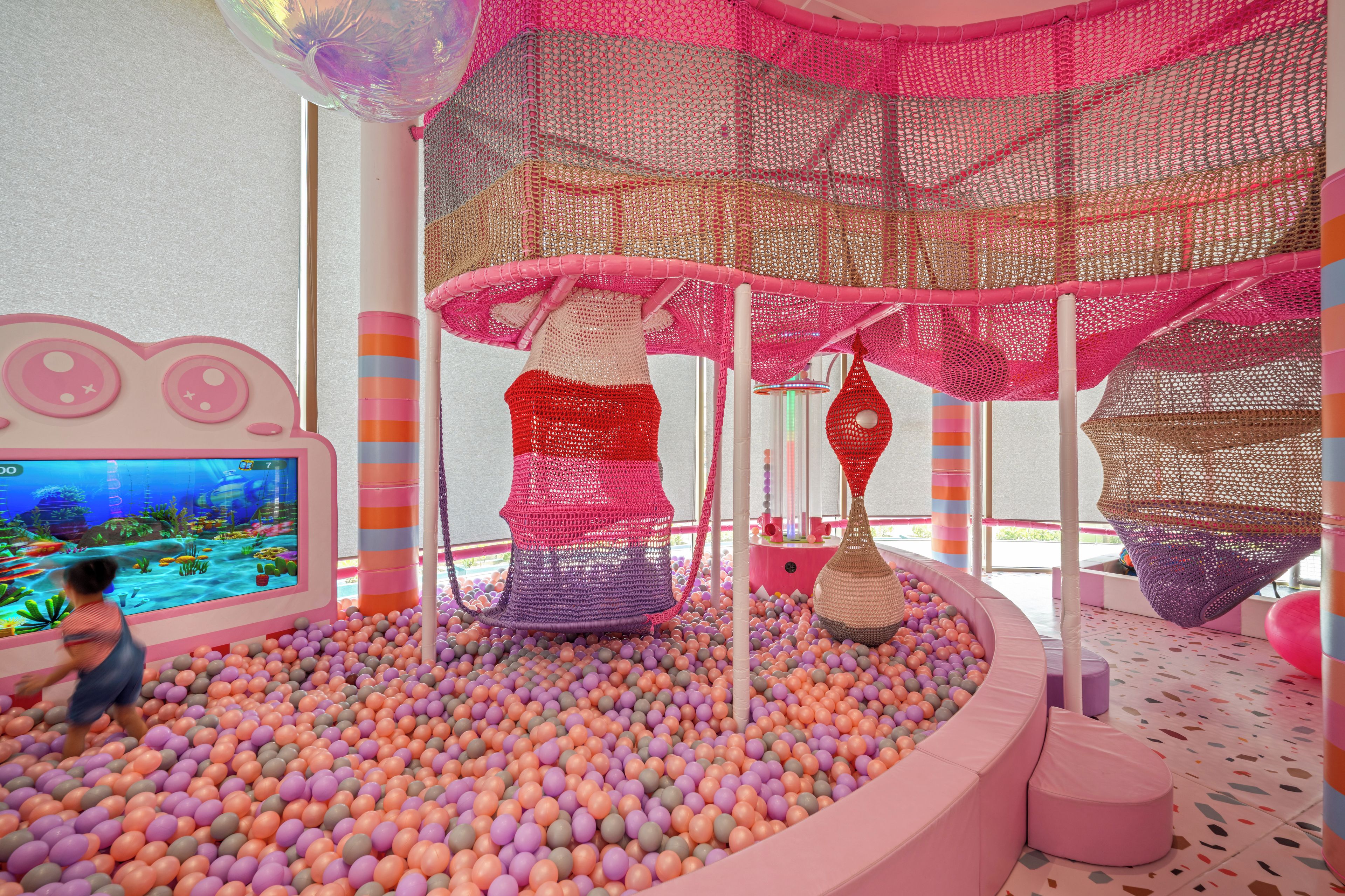 A play area with a ball pit, netted climbing structures, and a television screen.