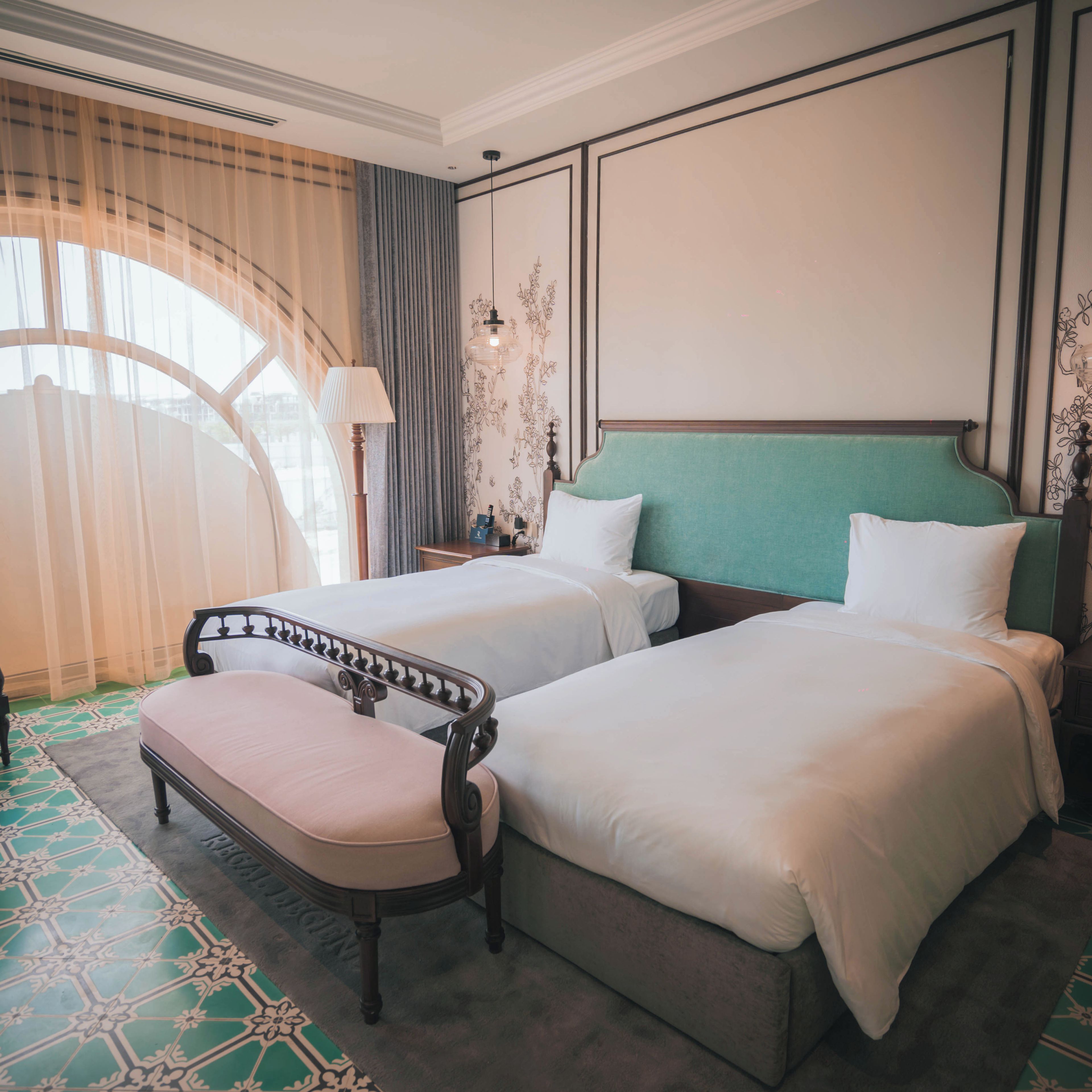 A hotel room with two beds, a bench, a lamp, and a decorative wall.