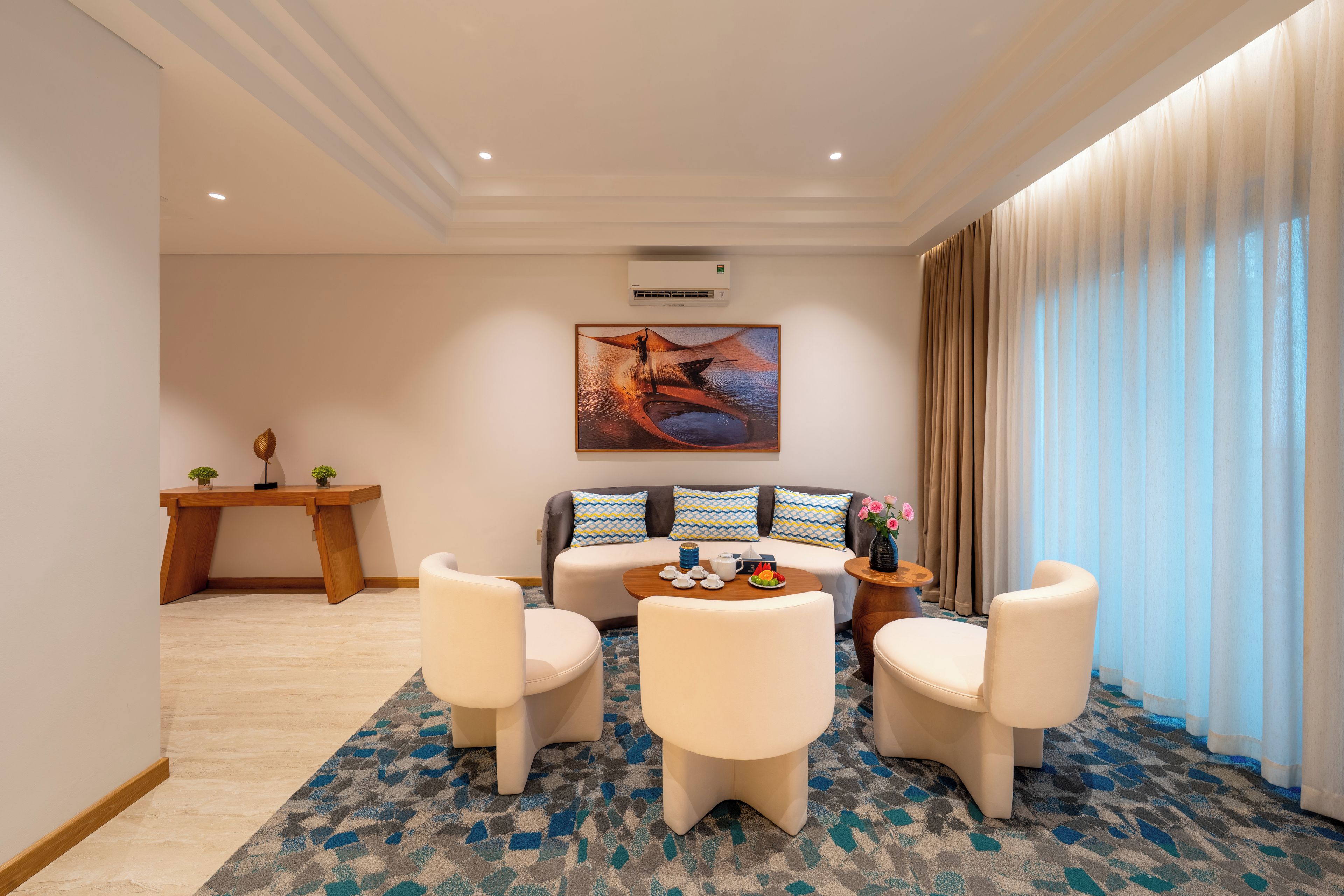 A modern hotel room with a sofa, two armchairs, a coffee table, and a dining table.