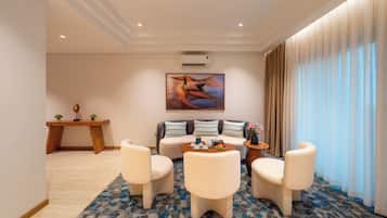 A modern hotel room with a sofa, two armchairs, a coffee table, and a dining table.