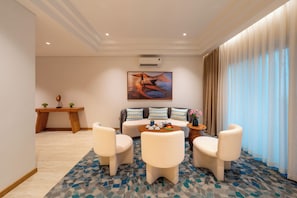 A modern hotel room with a sofa, two armchairs, a coffee table, and a dining table.