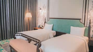 Ein Hotelzimmer mit zwei Betten, einer Bank, einem Nachttisch, einer Lampe und einer Wand mit Blumenmuster.