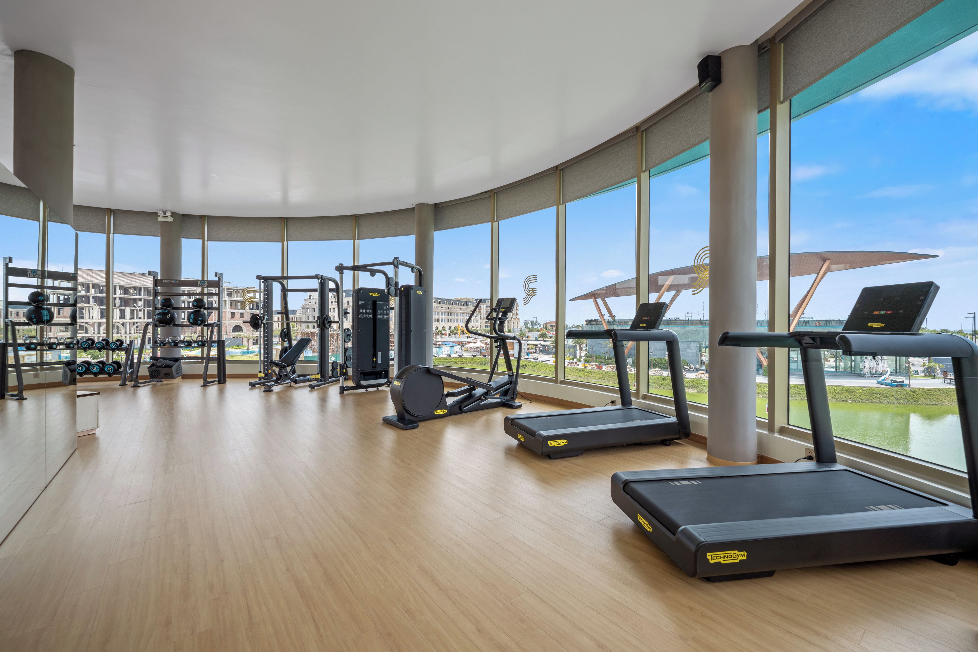 Ein Fitnessstudio mit unterschiedlichen Trainingsgeräten, großen Fenstern und Blick auf Gebäude.