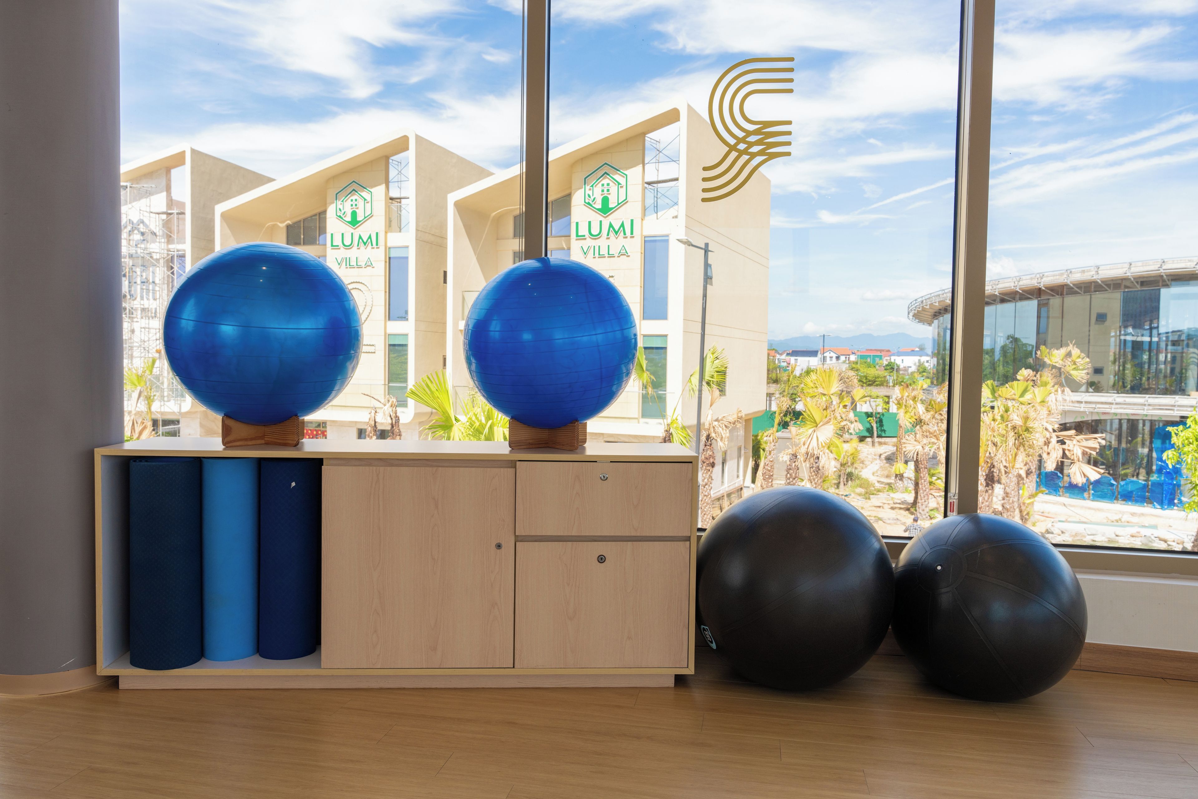 A room with exercise balls, a wooden cabinet, and a view of a building with 'LUMI VILLA' signage.