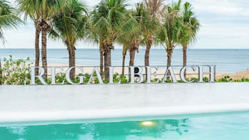 A sign with the text 'REGABEAH' in front of a pool with a view of the beach and ocean.