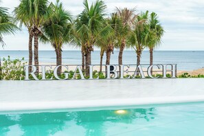 A sign with the text 'REGABEAH' in front of a pool with a view of the beach and ocean.