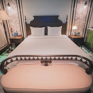 Una cama bien hecha con cabecera y piecera de madera, flanqueada por dos mesitas de noche con lámparas, en una habitación con papel tapiz estampado.