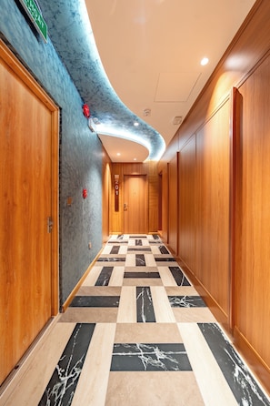 Pasillo de hotel con puertas de madera, suelo de mármol a cuadros e iluminación empotrada en un techo curvo.