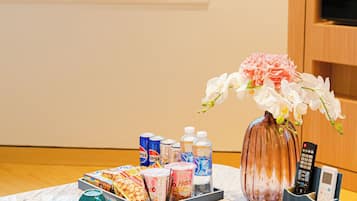 A hotel room with a marble table set with various amenities including a vase of flowers, a tray of snacks, and a remote control.