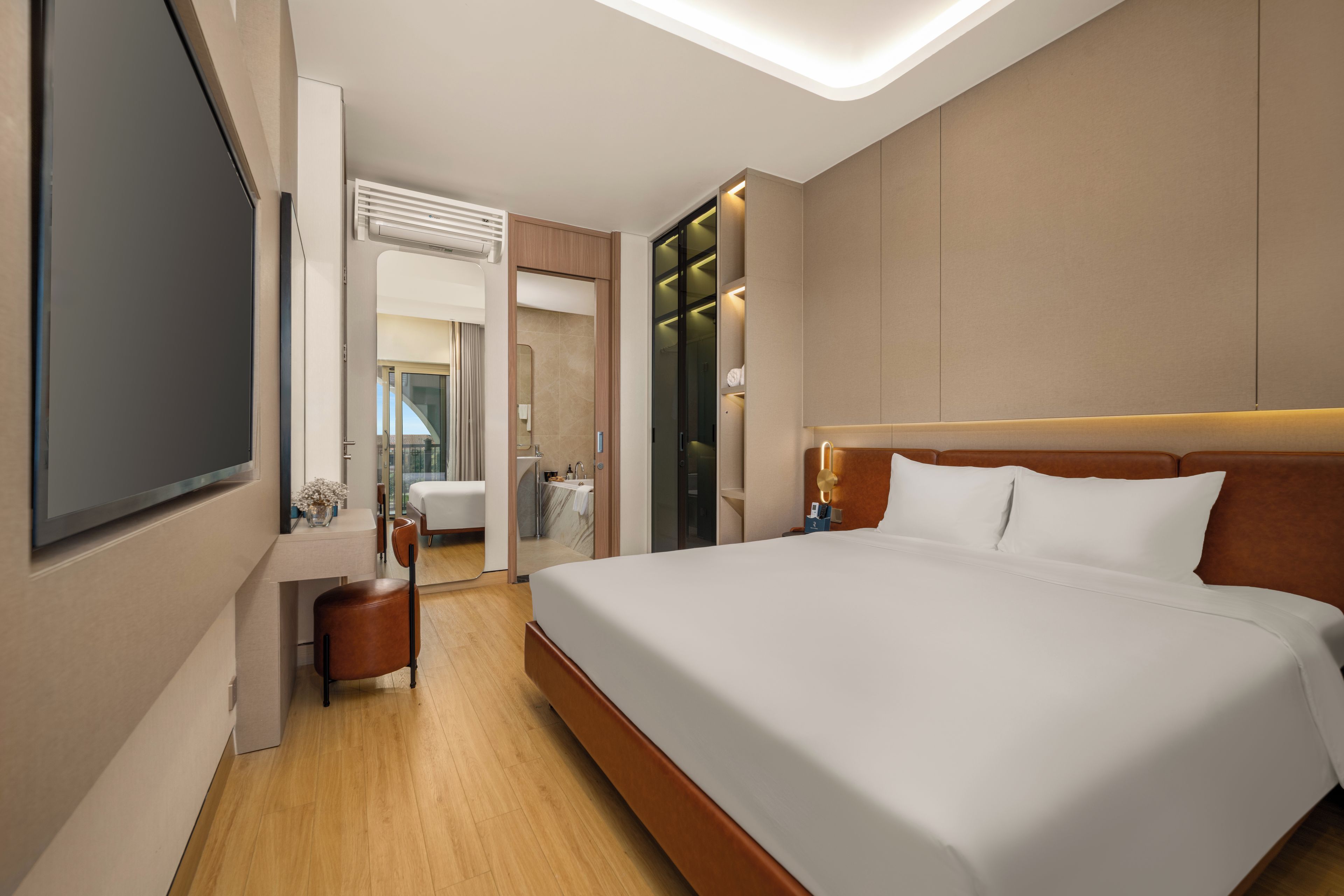 Une chambre d’hôtel avec un grand lit, un bureau, une chaise, une télévision et une salle de bain visible à travers une porte ouverte.