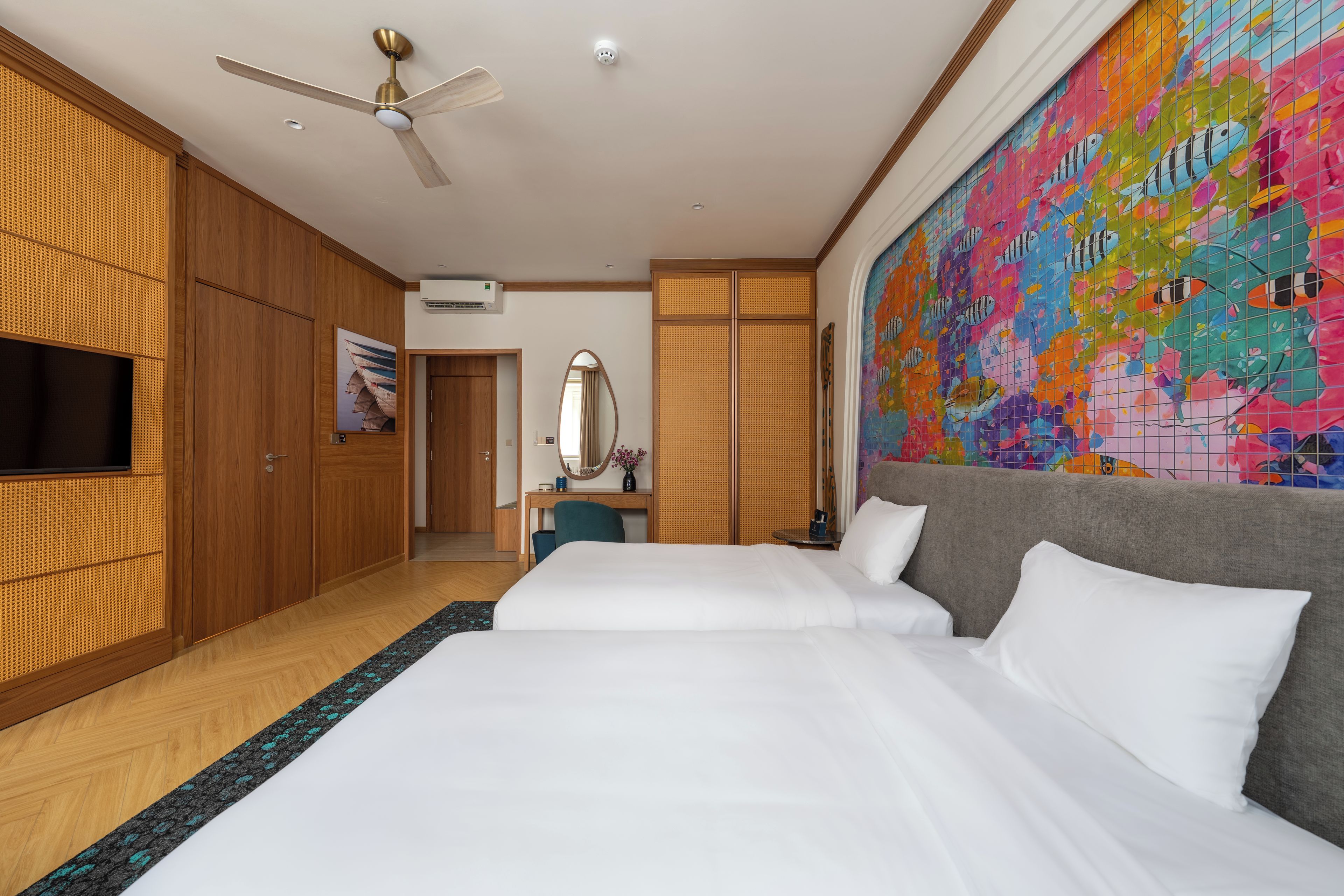 A hotel room with a bed, a desk, a television, and a colorful mural.