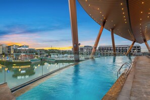 An indoor swimming pool with a view of the cityscape and a modern architectural structure with a wooden roof.